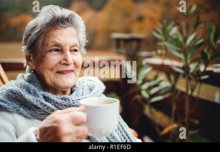 Una donna anziana in piedi all'aperto su una terrazza in una giornata di sole in autunno. Foto Stock