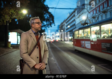 Imprenditore maturo con la valigia in attesa di un tram in serata. Foto Stock