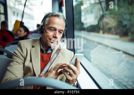 Coppia stanco imprenditore con cuffie e lo smartphone in viaggio in autobus in città. Foto Stock