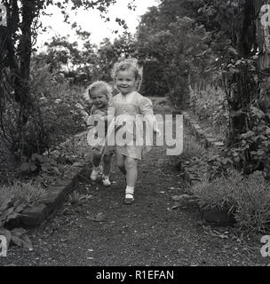 Degli anni Cinquanta, storico, due giovani ragazze a giocare insieme su un percorso di giardino, Inghilterra, Regno Unito. Foto Stock