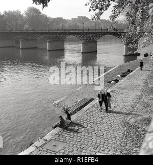 Degli anni Cinquanta, storico, diurno e una coppia di Parigi a piedi lungo un sentiero acciottolato accanto al fiume Senna, Parigi, Francia. Foto Stock