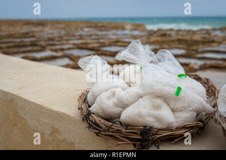 Salinas. Saline o salters in background con sacchetti di sale pronti per la vendita in un cestino o ciotola all'aperto. Raccolta a mano sale in Isola di Gozo Marsalforn Foto Stock