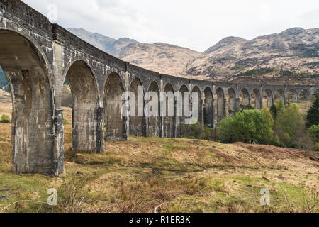 Vecchia Stazione ferroviaria ponte arcuato circondato da alberi con le colline in vista, Glennfinnan viadotto, Highlands Scozzesi. Tempo di primavera dell'anno Foto Stock