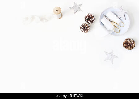 Natale craft, inverno di nozze composizione. Angolo decorativo pigne, nastri di seta, golden forbici sulla piastra di porcellana e stelle di legno. White ta Foto Stock