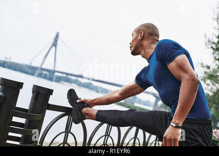 Vista laterale verticale di un africano sportive uomo che si allunga le gambe Foto Stock