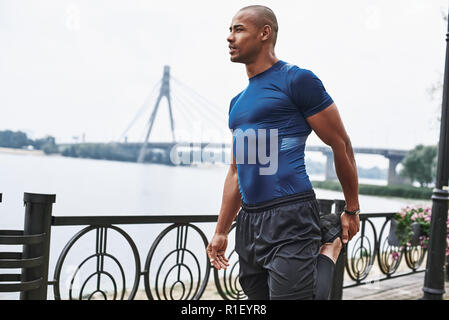 Vista laterale verticale di un africano sportive uomo che si allunga le gambe Foto Stock