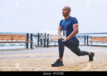 A piena lunghezza Ritratto di un africano sportive uomo che si allunga le gambe Foto Stock