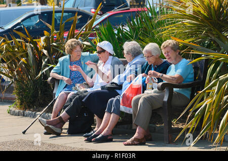 Cinque femmine pensionati seduti insieme su una panchina al sole, Eastbourne, England, Regno Unito Foto Stock