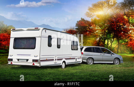 Il autotrailer sorge su un prato vedico prato nella foresta con una vista delle montagne. Inizio autunno con red e delta alberi. La famiglia è andato su vaca Foto Stock