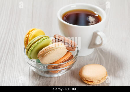 Amaretti gustosi dolci di diverso colore in recipiente di vetro e la tazza di caffè su schede di colore grigio Foto Stock