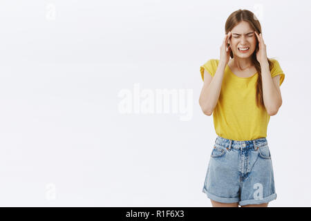 Intensa bella caucasica donna slim in giallo maglietta e pantaloni corti denti di aggraffaggio chiudendo gli occhi e accigliata tenendo le mani sulle tempie sensazione unfo Foto Stock