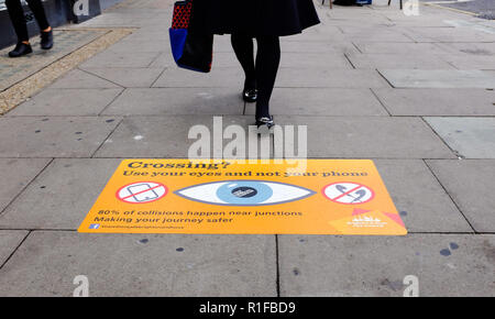 Pavimentazione stradale segni chiedendo ai pedoni di prendersi cura di attraversare la strada e non guardare i loro telefoni cellulari per ascoltare la musica su cuffie a Brighton Regno Unito Foto Stock