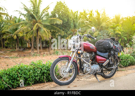 Una vecchia motocicletta pranzo e parcheggiata accanto a palme su una piccola strada Foto Stock