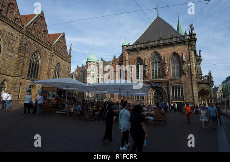 Marktplatz, Bremen. Deutschland La Germania. Una scena che si affaccia su piazza del mercato cercando su uno spazio esterno riservato per servire i rinfreschi per drink e pasti leggeri. Molte persone stanno godendo i rinfreschi mentre altri a piedi da. Grandi ombrelloni proteggerli dagli elementi che si tratti di pioggia o sole forte anche se è attualmente sotto l'ombra. Foto Stock