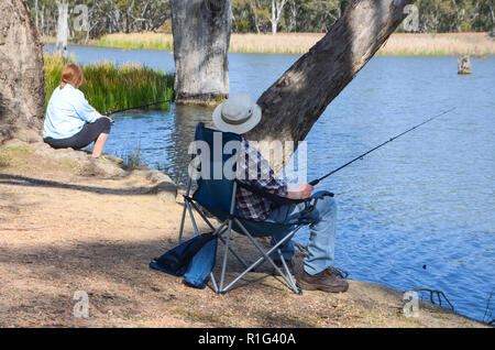 Coppia maschio e femmina di sedersi sulla banca del fiume di pesca. Adulto anglers godere un momento di relax di pesca. Foto Stock