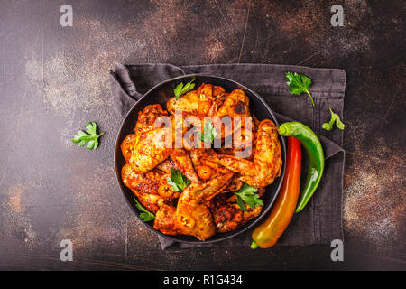 Fritti speziati ali di pollo in salsa di paprika in una piastra nera su sfondo scuro, vista dall'alto, copia dello spazio. Foto Stock