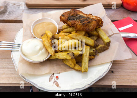 Pesce e patatine fritte servite con curry e salsa tartara su una piastra con un foglio di carta. Si tratta di un piatto caldo di origine inglese costituito da frittura di pesce martoriato e ho Foto Stock