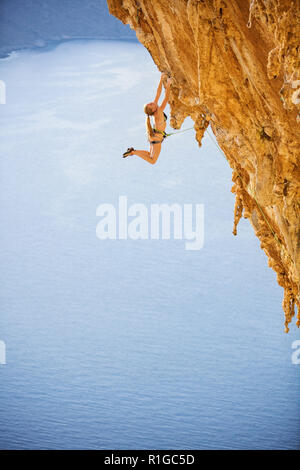 Femmina di rocciatore saltando sulle maniglie sul tracciato impegnativo sulla scogliera, Kalymnos Island, Grecia Foto Stock