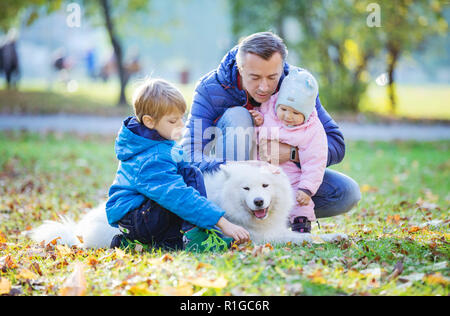 Padre con figlio di età prescolare e baby figlia gioca con il suo cane samoiedo in autunno park Foto Stock