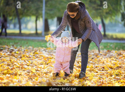 La madre del bambino di supporto figlia e di aiutarla a fare i primi passi. Mamma e figlia sulla passeggiata nel parco d'autunno. Foto Stock