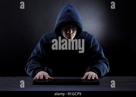 Hacker nel cofano e bicchieri di fronte ad una tastiera su uno sfondo scuro Foto Stock