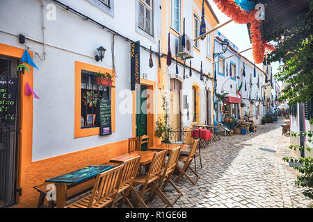 Terrazze dei ristoranti in un vicolo lastricato di Ferragudo village, regione di Algarve, PORTOGALLO Foto Stock
