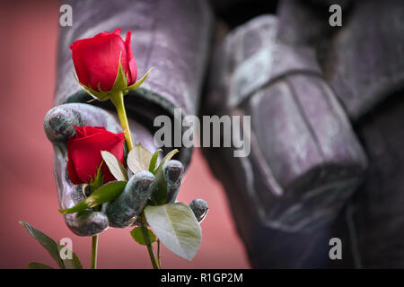 Close up Roses sulla statua di soldato. Rose rosse su una chiusura di una statua di una guerra mondiale un soldato. Foto Stock