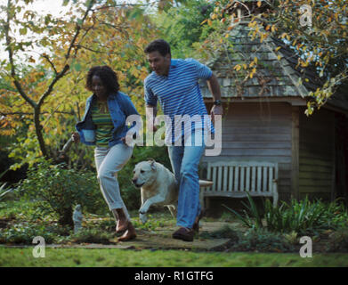 Felice mid-adulto giovane in esecuzione con il loro cane nel cortile di casa propria. Foto Stock