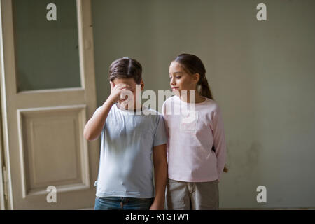 Ragazzo che copre la sua gli occhi e sorridere mentre la sorella si affaccia su di una stanza. Foto Stock