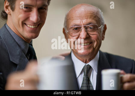 Ritratto di un sorridente senior business man con una tazza di caffè mentre un mid-adulto collega solleva un toast. Foto Stock