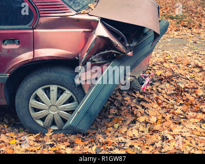 Parte posteriore della vettura dopo il crash incidente. closeup side shot di fracassato accartocciata paraurti posteriore e il pneumatico sgonfio. autunno autunno. strada coperta di caduti y Foto Stock