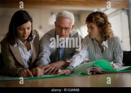 Adulto Uomo d'affari alla ricerca di documenti con metà femmina adulta colleghi in un ufficio. Foto Stock