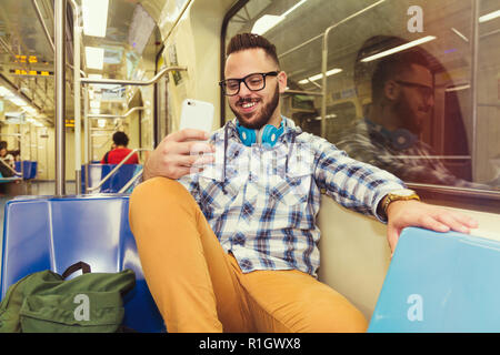 Giovani traveler indossando plaid shirt e bicchieri di leggere il divertimento di feed sui social network pagine su telefono cellulare sulla metropolitana di trasporto pubblico. Concetto di co Foto Stock