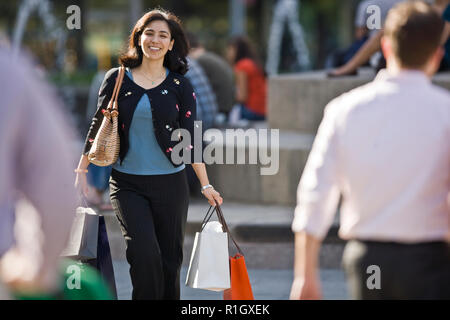 Sorridente metà donna adulta il trasporto delle borse della spesa mentre si cammina attraverso la città. Foto Stock