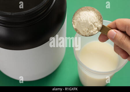 La proteina del siero di latte integratore alimentare per la formazione e l'esercizio. Shaker con il latte. Prospettiva, tenendo misurino pieno di aroma di vaniglia in polvere su verde Foto Stock