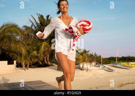 Donna sorridente in esecuzione sul pontile in legno tenendo un striped telo da spiaggia. Foto Stock