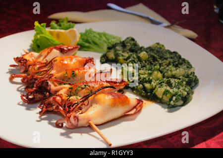 Calamari, calamari con limone e verdure, patate sulla piastra bianca con il tessuto e il coltello Foto Stock