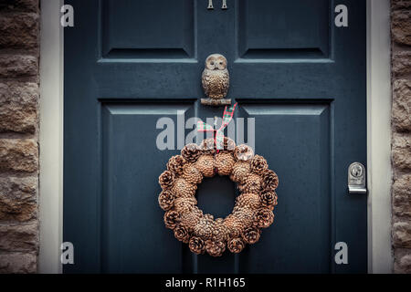 Close-up di Natale corona di coni fir attaccato ad una vecchia porta blu di una pietra costruito casa. Foto Stock