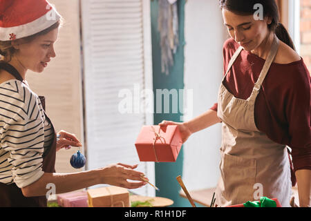 Ritratto di due sorridenti giovani donne natale di imballaggio presenta in art studio, spazio di copia Foto Stock