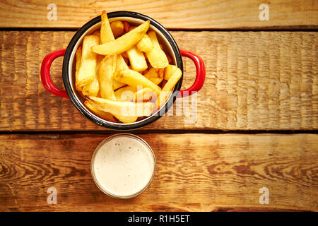 Vista dall'alto di deliziose patatine fritte in un recipiente rosso con salse su un vecchio tavolo in legno Foto Stock