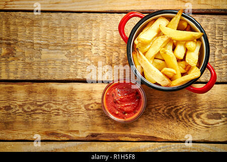 Vista dall'alto di deliziose patatine fritte in un recipiente rosso con salse su un vecchio tavolo in legno Foto Stock