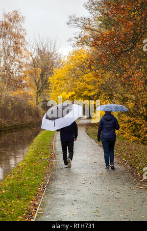 Coppia che cammina lungo il sentiero del canale Llangollen sotto la pioggia sotto ombrelloni Foto Stock