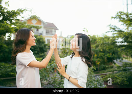 Due belle giovani donne dando alta cinque - belle ragazze in piedi sul all'aperto e divertirsi - migliori amiche facendo una promessa Foto Stock