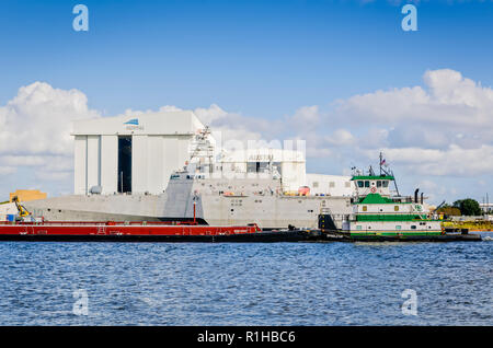 La M/V Spindletop towboat, possedute da Higman servizi nautici, spinge una chiatta passato la USS Gabrielle Giffords (LCS 10) sul Fiume Mobile, 27 novembre Foto Stock