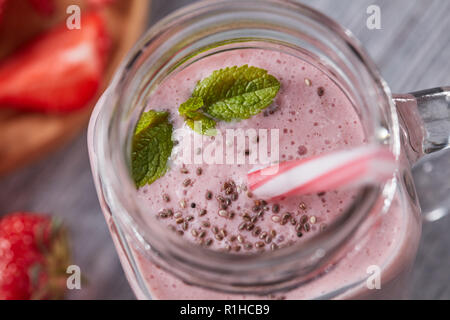 Primo piano di un preparato di fresco latteo-vitamina berry smoothie con chia semi e foglie di menta su un grigio Sfondo di legno. Vista superiore Foto Stock