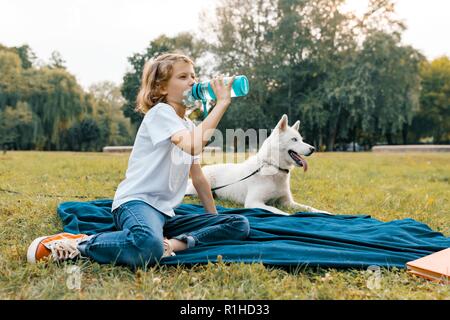 Bambina con cane bianco Husky nel parco si siede sul prato, gioca e legge di riposo. Foto Stock