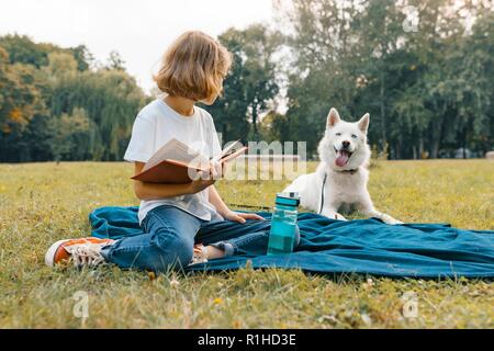 Bambina con cane bianco Husky nel parco si siede sul prato, gioca e legge di riposo. Foto Stock