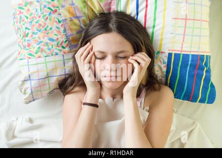 Close-up viso della ragazza adolescente sul cuscino con gli occhi chiusi tenendo la testa con le mani. Foto Stock