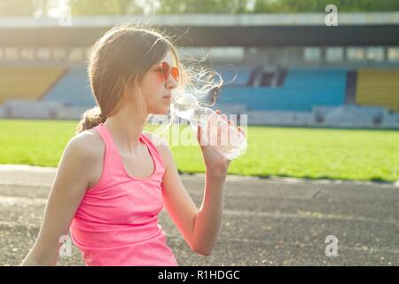 Bella ragazza adolescente riposo dopo allenamento allo stadio, ragazza sedette per rilassarsi, acqua potabile. Foto Stock