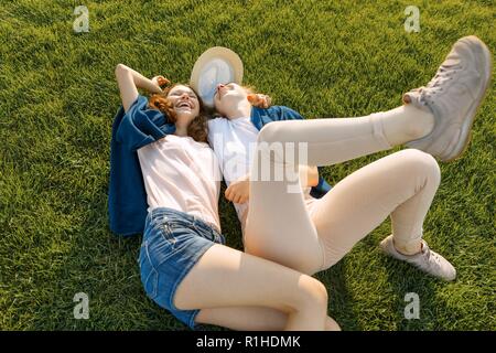 Due giovani ragazze sorridenti amici giacciono abbracciando sull'erba verde in estate soleggiato parco, vista dall'alto, le ragazze sono il divertimento in estate giornata di sole. Foto Stock